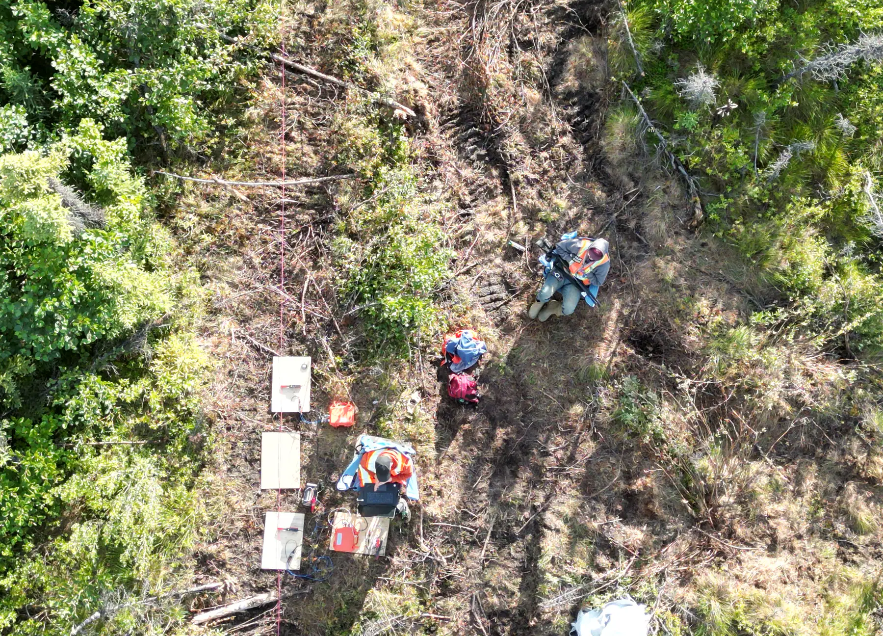 A Rosor crew on a cut line seen from above, setting up a ground transmitter with the survey wire running out of frame