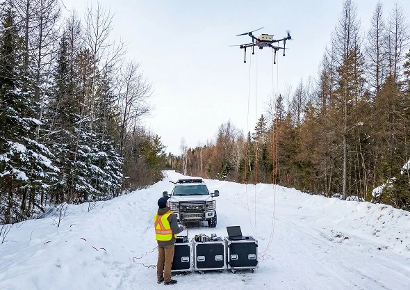 A Rosor Recon Super in flight above a snow-covered access line, with a single operator monitoring the survey from a laptop and equipment cases on the ground