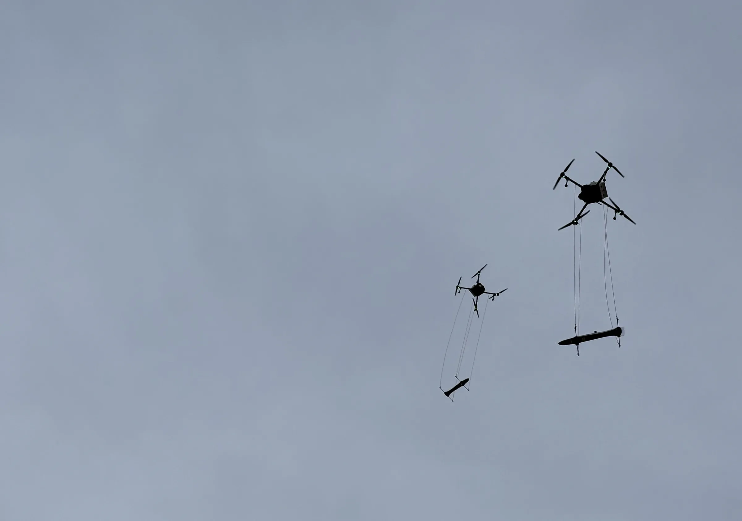 Two Rosor survey drones in flight, each carrying a sensor slung beneath it